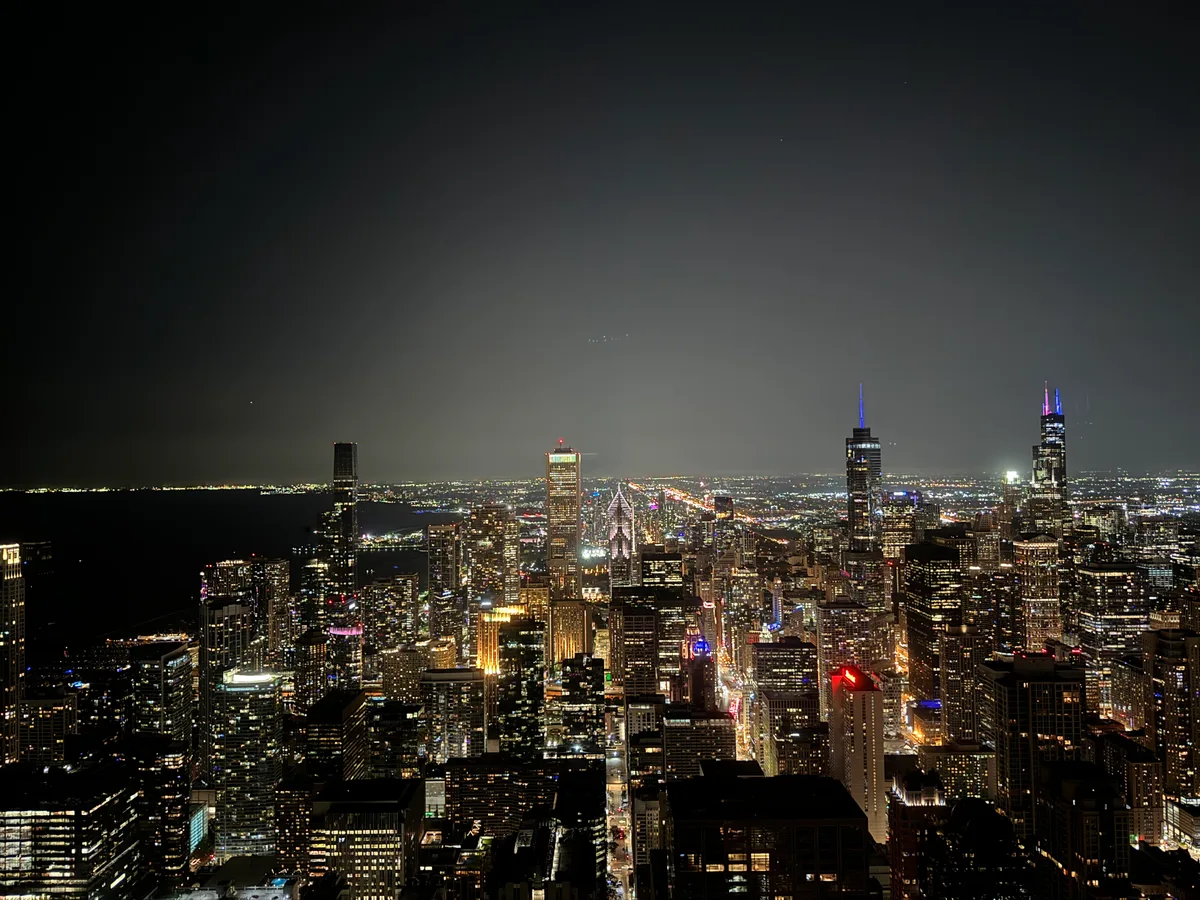 Panoramic night view of Chicago, Illinois skyline with illuminated skyscrapers including Willis Tower, and city lights stretching to the horizon above Lake Michigan