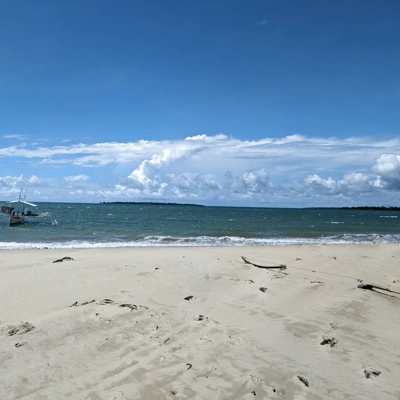 Sandy Palawan beach with a traditional outrigger bangka boat in the foreground under a cloudy sky, Caramay area
