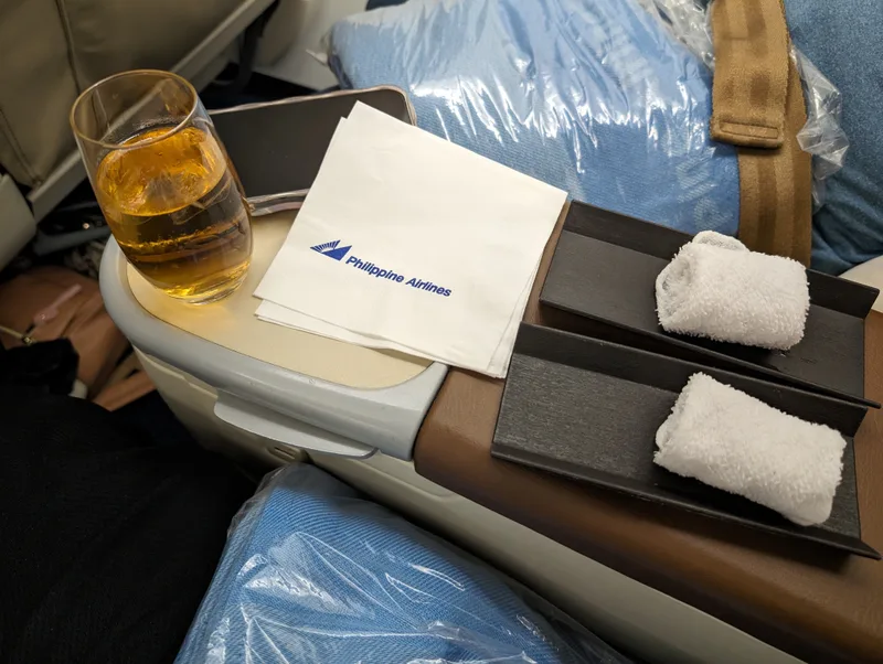 Philippine Airlines business class tray with amber drink and white cocktail napkins on the tray table