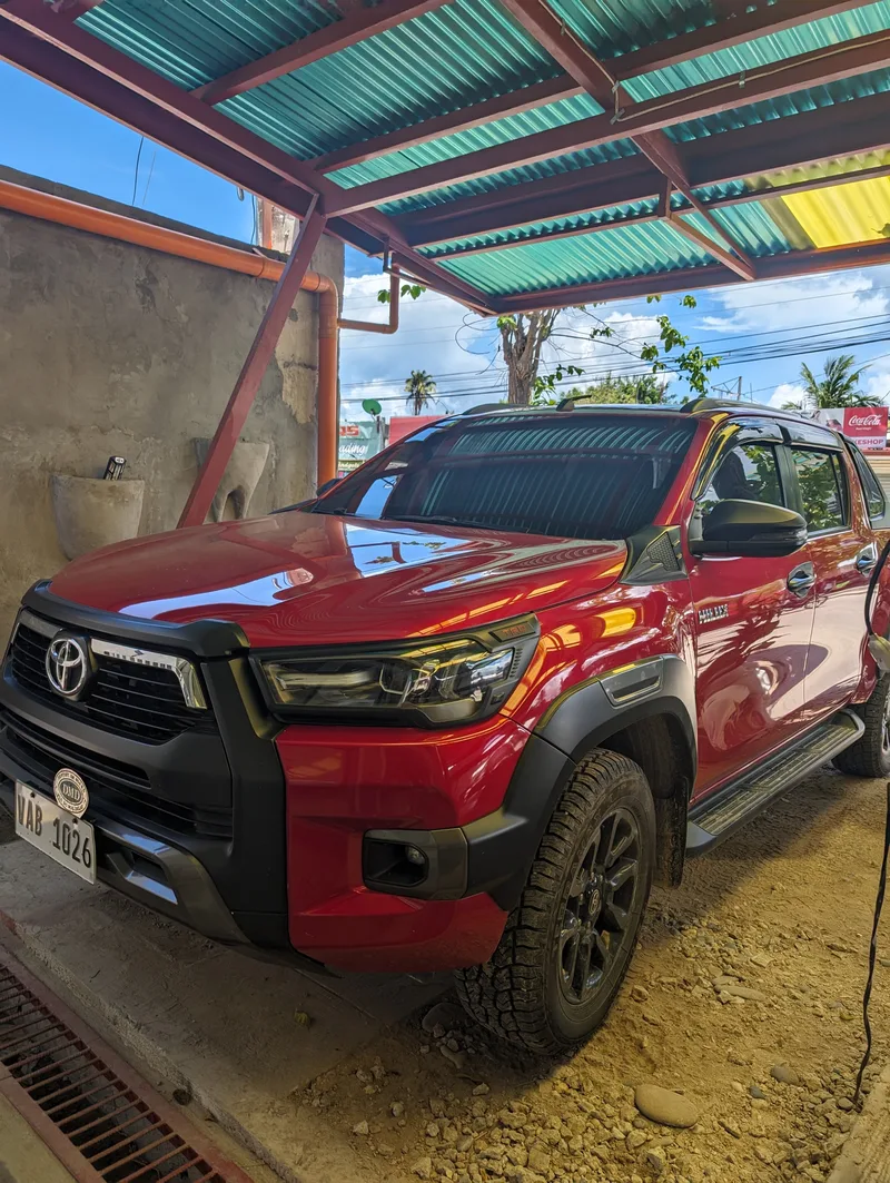 Shiny red Toyota Hilux Conquest pickup truck parked under a corrugated metal roof at a dental clinic in Roxas, Palawan