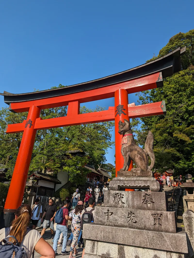 Large red torii gate and stone fox statue at a Japanese shrine entrance in Kyoto, Japan.