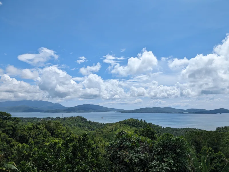 Panoramic view of a bay dotted with islands surrounded by lush green hills under a bright blue sky with white clouds on the road between Sabang and Puerto Princesa, Palawan, Philippines