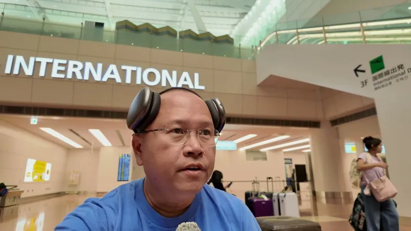 Man with headphones standing in front of the INTERNATIONAL sign at Haneda Airport terminal, Tokyo, Japan