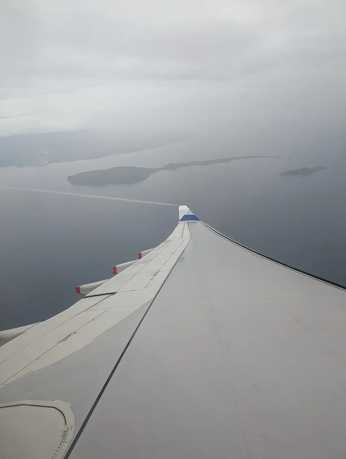 Aerial view from airplane wing over water and distant islands under hazy sky