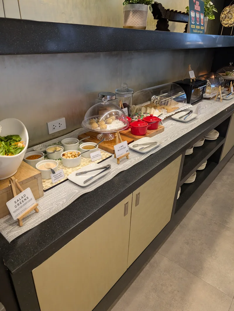 Airport lounge food spread with salad greens, muffins, and various dishes at Ninoy Aquino International Airport in Manila, Philippines.