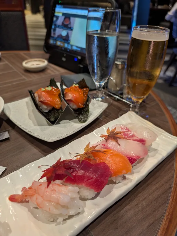 Assortment of fresh sushi and sashimi with nigiri, salmon roe hand rolls, and maple leaf garnish next to a glass of beer at a Shibuya restaurant in Tokyo, Japan