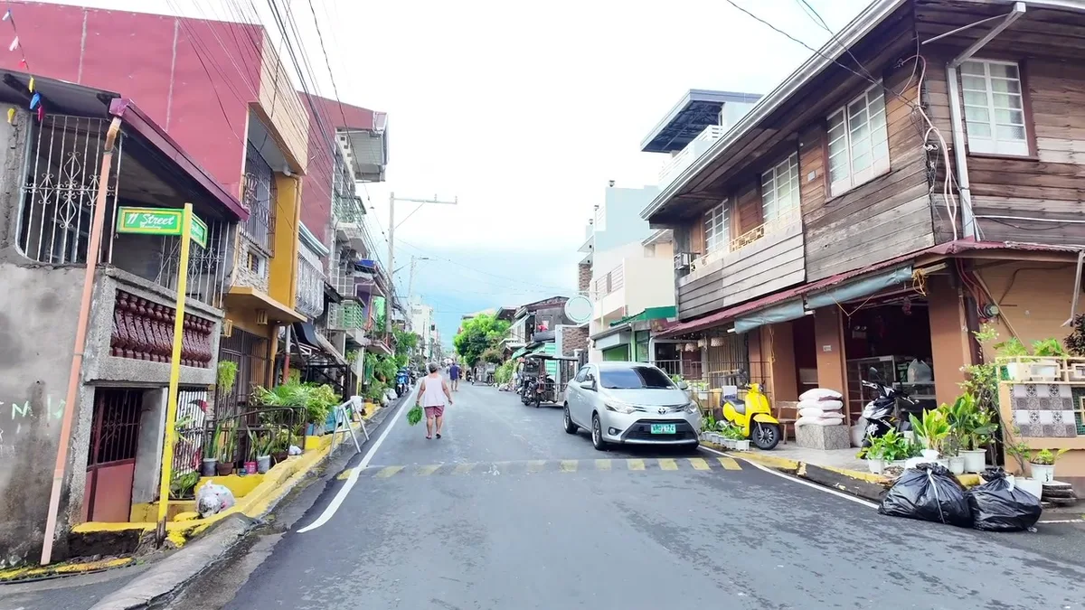 Narrow street in the Philippines lined with colorful buildings and parked vehicles, a person walking.