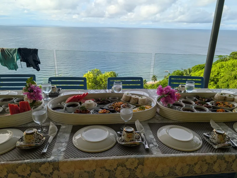Two large oval platters of breakfast food with rice, eggs, and fruit on an outdoor table with the ocean in the background at Casa Amara, Batangas, Philippines.