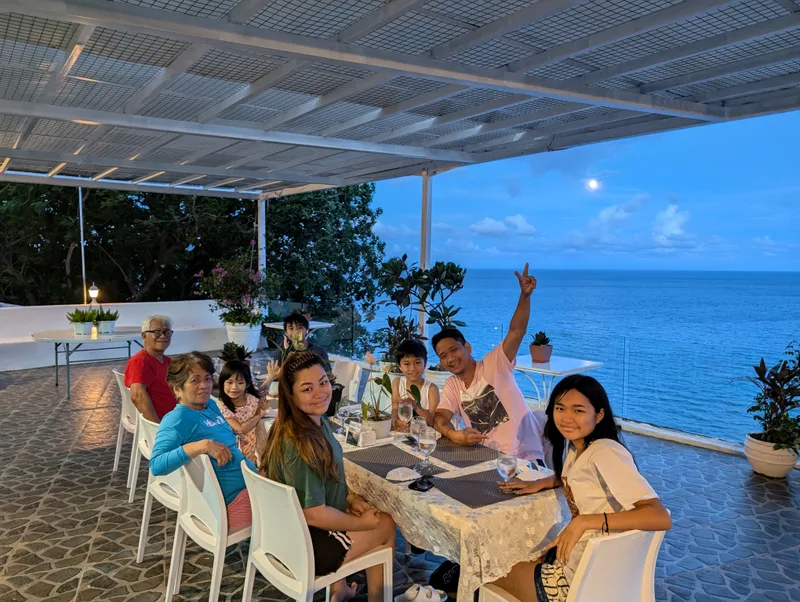 Family seated at an outdoor patio table under a full moon with the moonlit ocean visible behind them at Casa Amara, Batangas, Philippines.