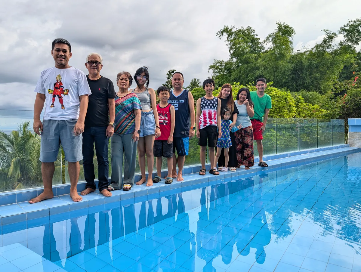 Family group of eleven people standing barefoot at the edge of an infinity pool with a panoramic ocean view under a cloudy sky at Casa Amara, Batangas, Philippines.