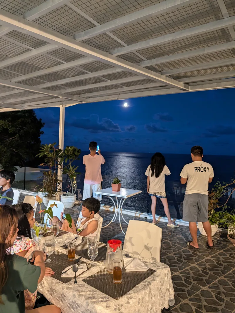 People at the edge of an outdoor patio photographing a full moon reflecting brightly on the dark ocean at night at Casa Amara, Batangas, Philippines.