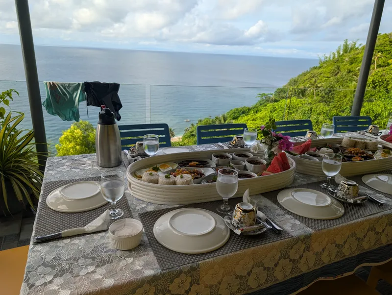 Outdoor dining table with breakfast platters set up overlooking the ocean and green hills at Casa Amara, Batangas, Philippines.