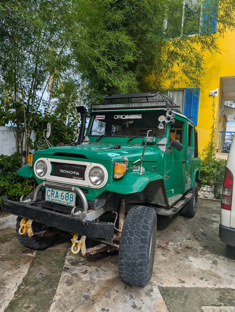 Bright green vintage Toyota Land Cruiser with roof rack, snorkel, and large off-road tires parked in front of a yellow building with bamboo at Casa Amara, Batangas, Philippines.