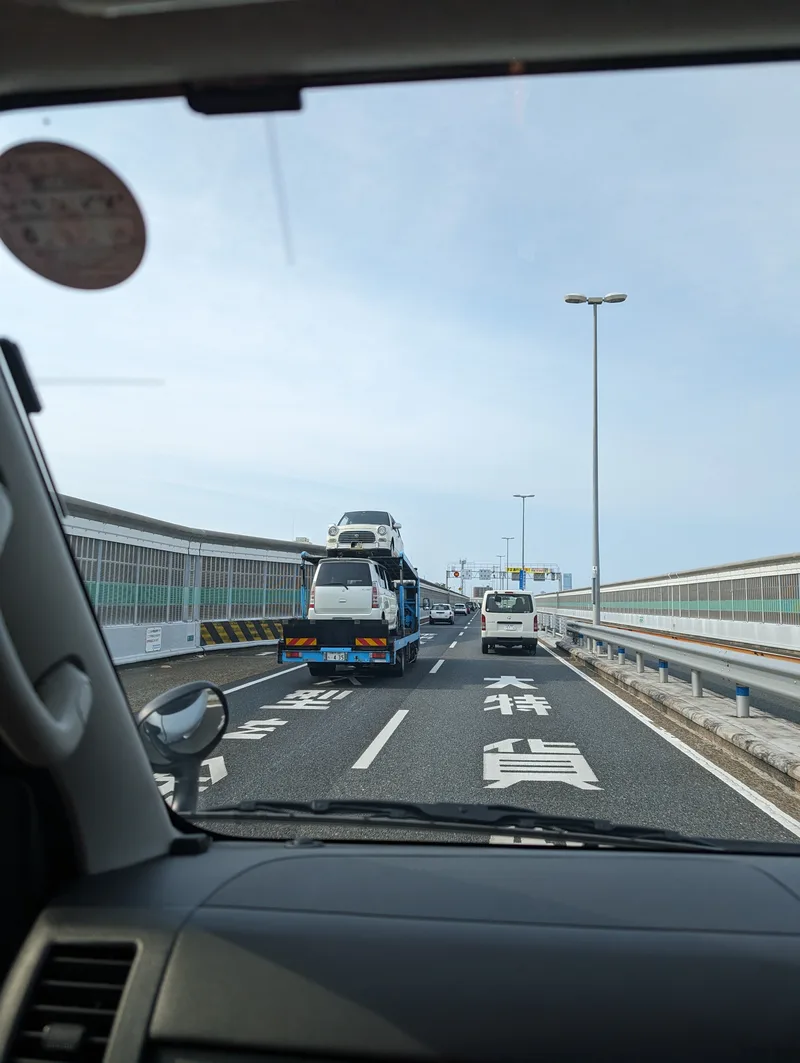 Car carrier truck transporting two white SUVs on a Japanese highway in Osaka.