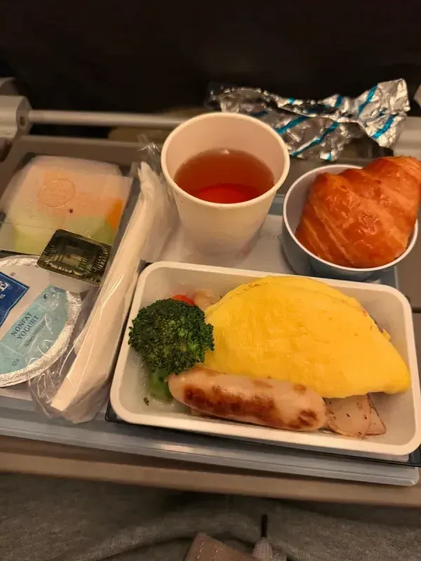 Airplane food was... okay Airplane breakfast with omelet, sausage, croissant, yogurt, and tea