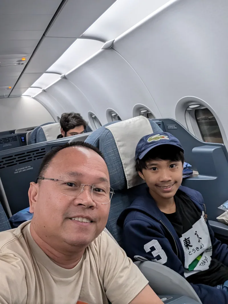 Man and his young son smiling for a selfie in the business class cabin of a Philippine Airlines flight from Tokyo Haneda Airport, Japan.