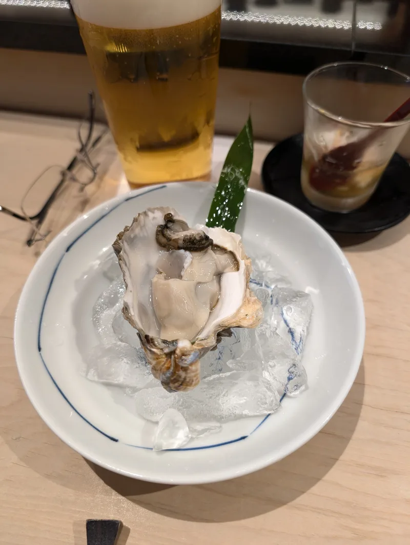 Fresh oyster served on a bed of ice in a white and blue rimmed bowl, garnished with a green leaf, at an omakase restaurant in Shibuya, Tokyo, Japan.