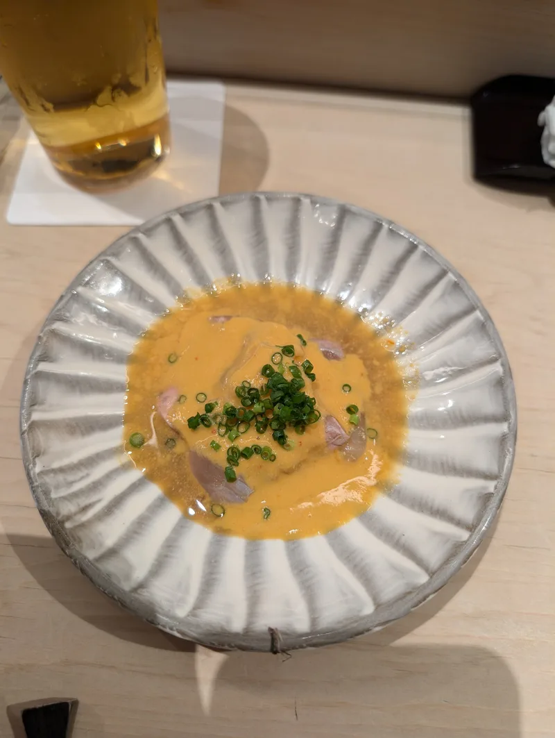 Raw seafood covered in a creamy orange sauce topped with chopped green onions, served in a decorative ceramic bowl at an omakase restaurant in Shibuya, Tokyo, Japan.