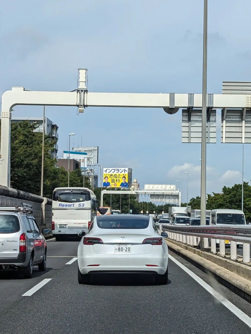 White Tesla on a multi-lane Tokyo expressway in Japan under a clear blue sky.