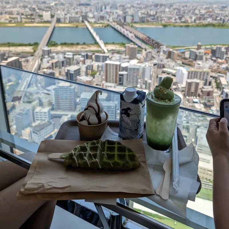 Matcha cream soda and matcha croffle desserts on a table with Osaka city view through window, Japan.