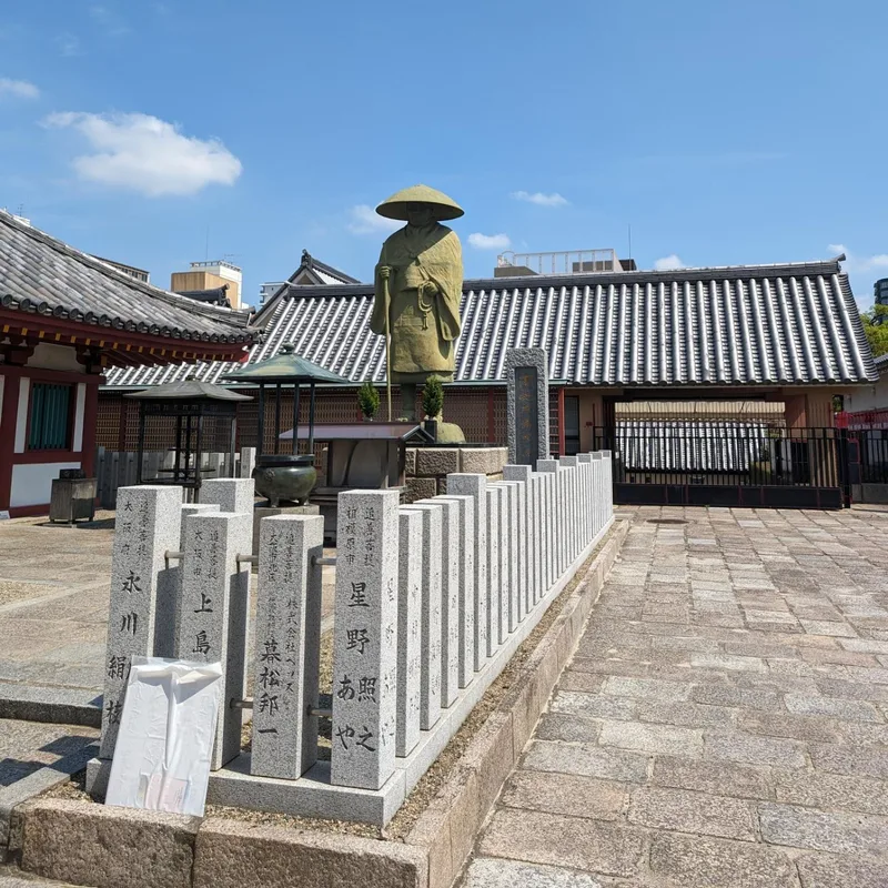 Stone statue of robed figure with conical hat in courtyard at Shitennoji Temple in Osaka, Japan.