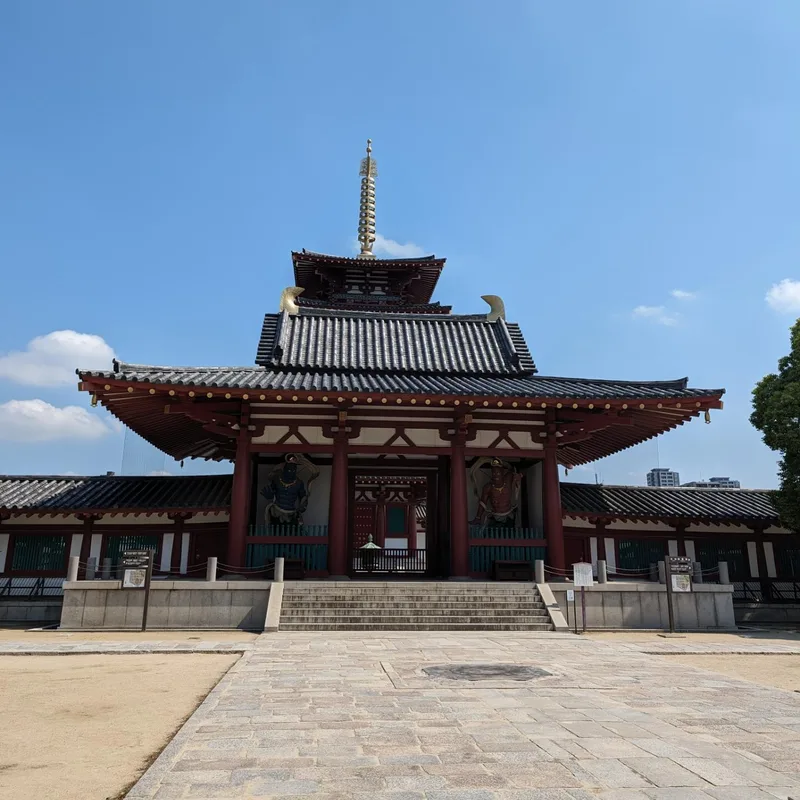 Main hall of Shitennoji Temple with golden spire and guardian statues under blue sky in Osaka, Japan.