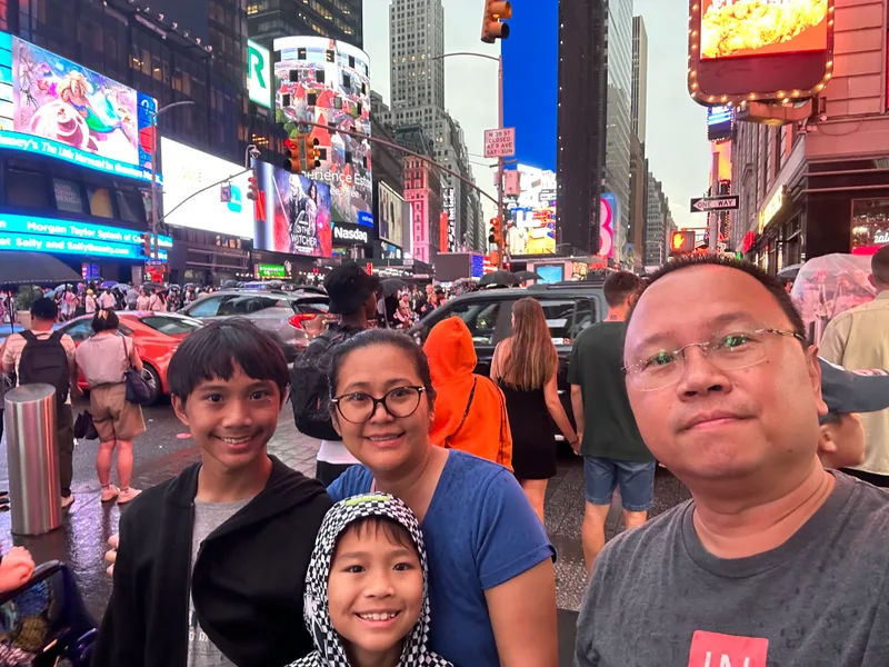Our first look at Times Square Family selfie in Times Square with bright billboards and skyscrapers