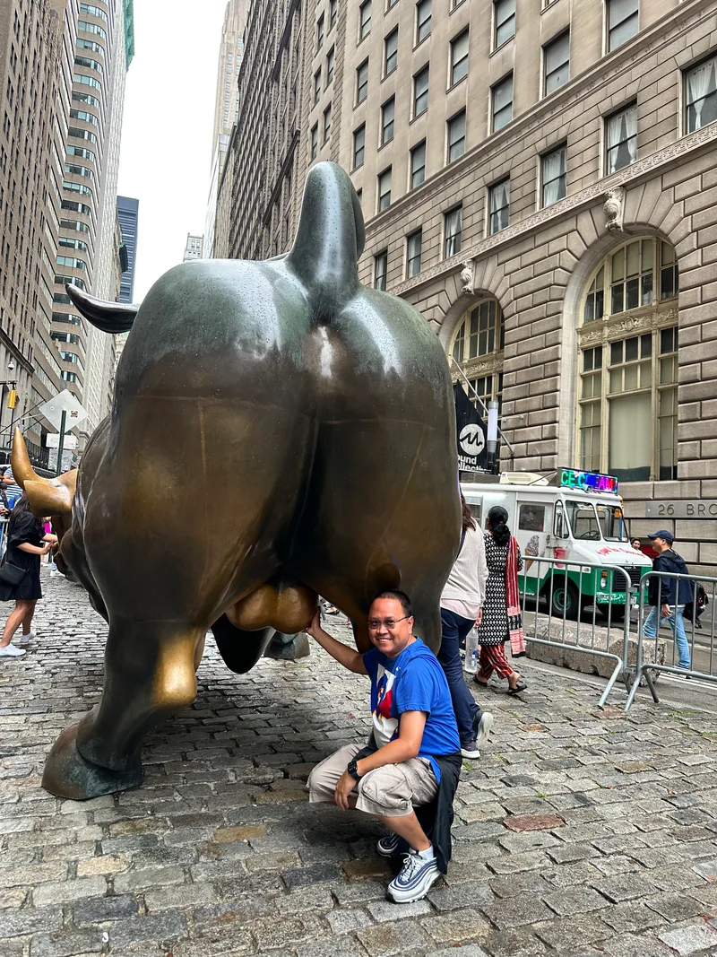 Getting all the luck I can — both hands Man smiling while touching Charging Bull statue on Wall Street