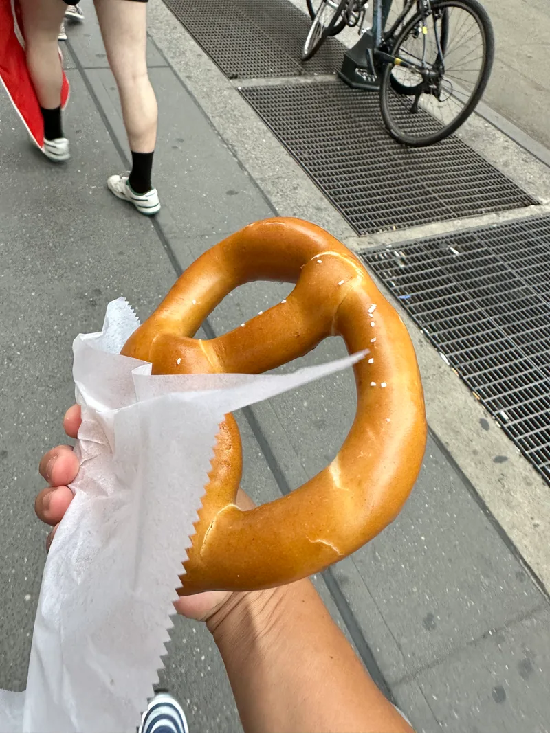 You can't visit NYC without trying a street pretzel Hand holding a large salted soft pretzel on a New York City street
