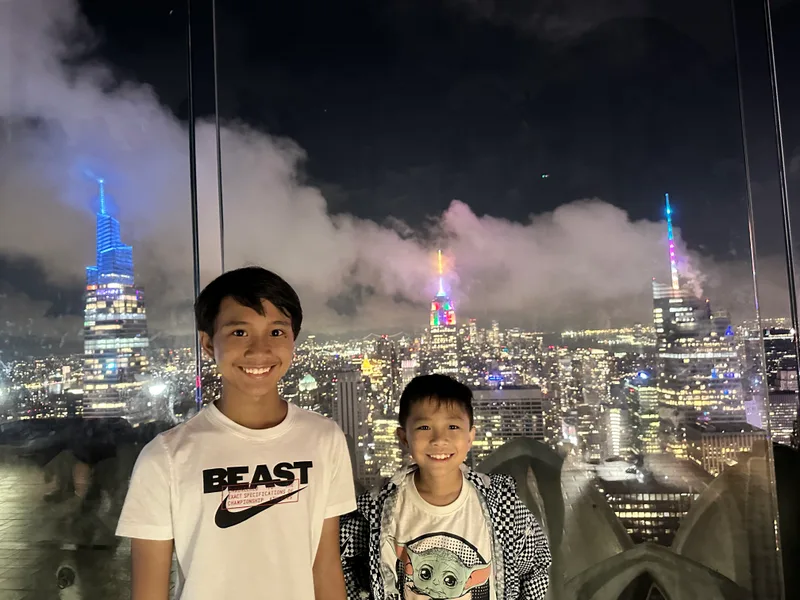 Two boys on NYC rooftop with illuminated skyline and Empire State Building