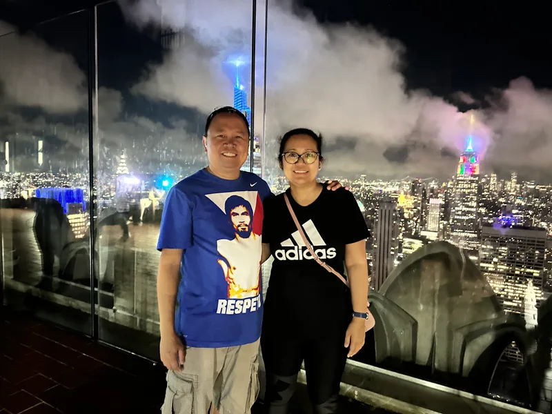 Top of the Rock — that skyline at night is unreal Couple on NYC rooftop with illuminated skyline and Empire State Building at night