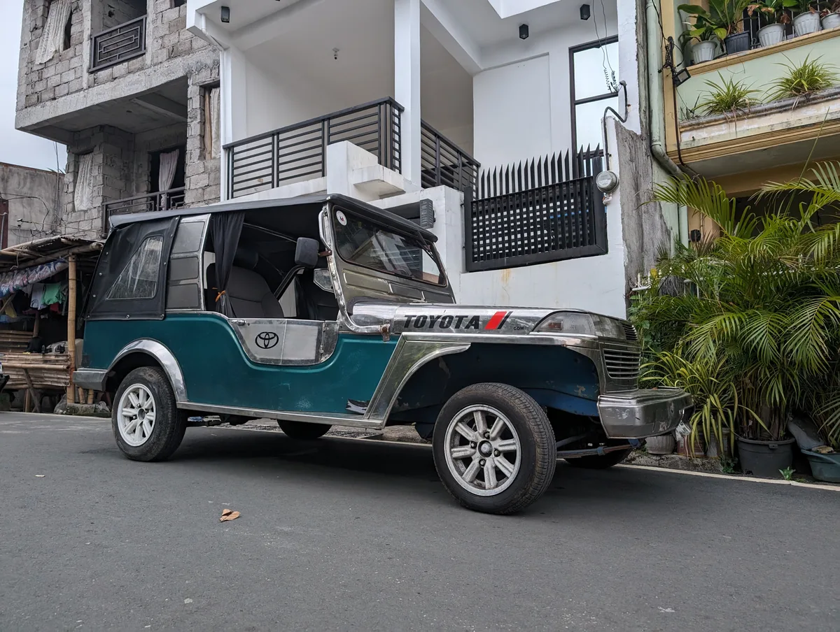 Teal and silver Owner Type Jeep parked on a street in Liliw, Laguna, Philippines in front of a modern white house.