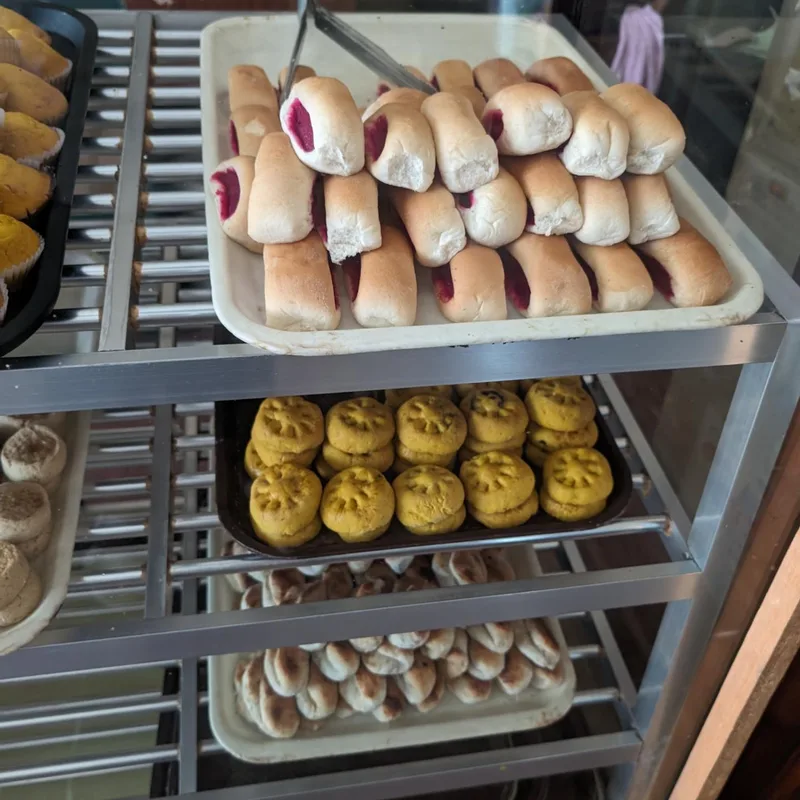 Multi-tiered bakery display case with jam rolls, yellow flower-shaped cookies, and small buns inside Modern Bakery in Roxas Palawan Philippines