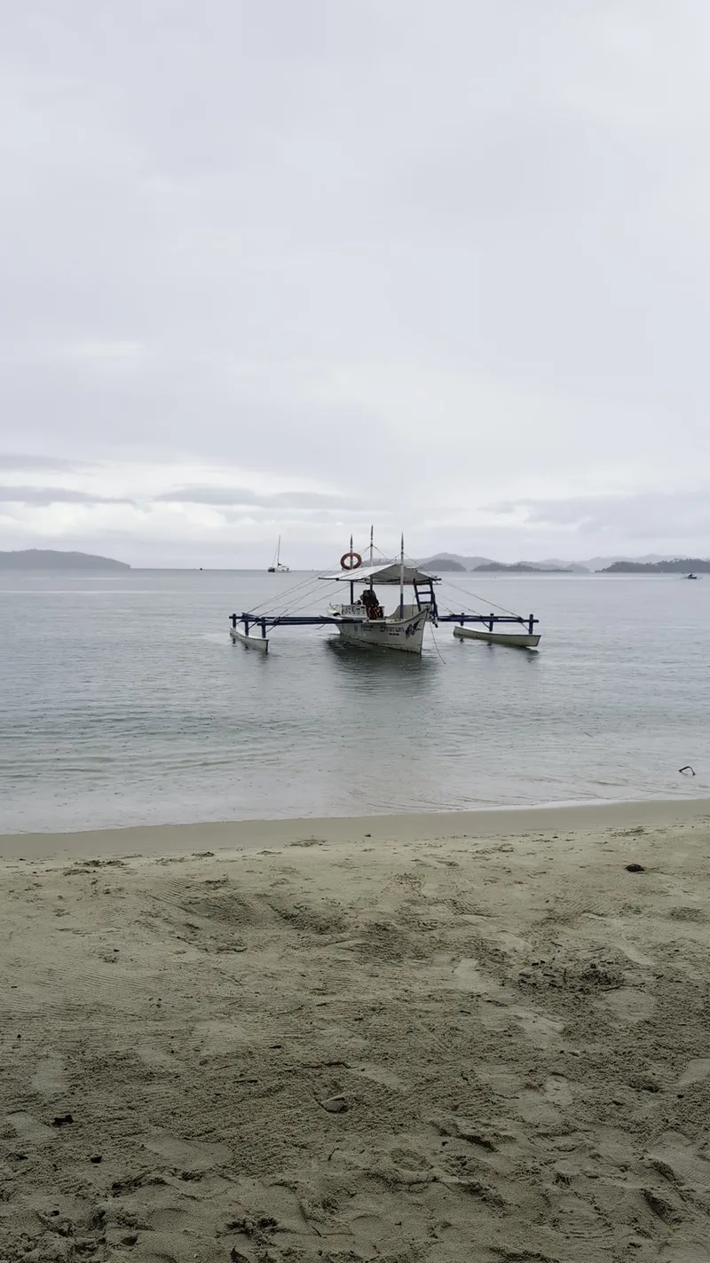 Traditional Filipino outrigger boat anchored near a sandy beach at Port Barton Palawan under an overcast sky