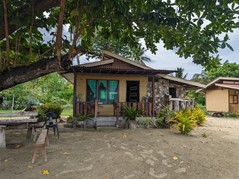 Small yellow cottage with stone facade and wooden porch surrounded by tropical plants at Henalric resort in Caramay, Roxas, Palawan