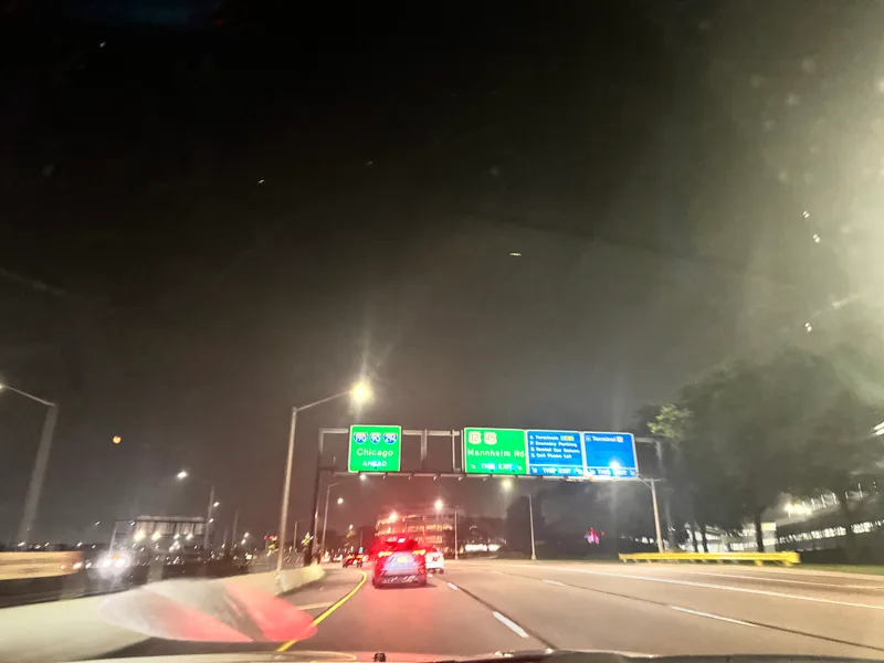 Nighttime highway view driving into Chicago, Illinois, showing illuminated "Chicago Ahead" road sign with car taillights ahead