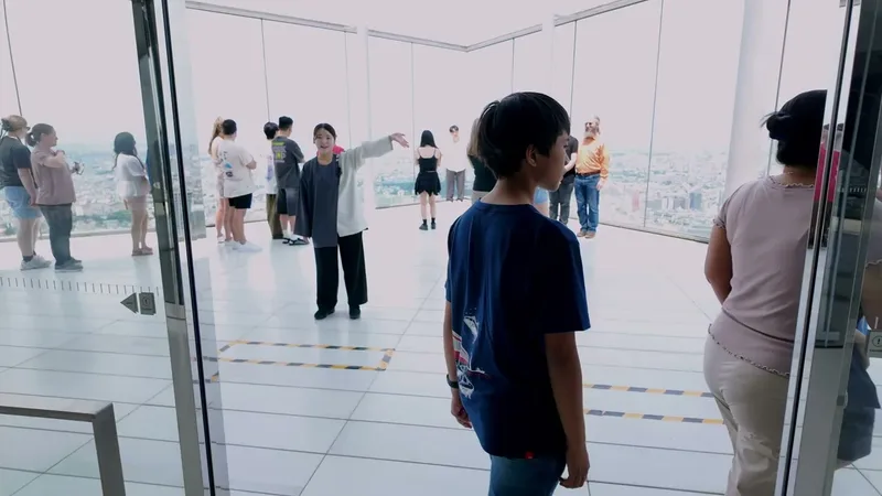 People inside the Shibuya Sky observation deck looking at the Tokyo, Japan city skyline through glass windows, a young boy in a blue shirt in the foreground.