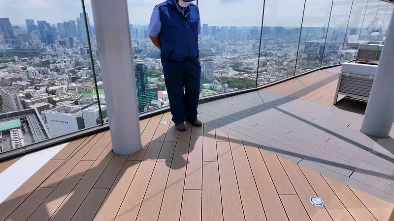 Staff member in blue uniform on the Shibuya Sky outdoor rooftop deck in Shibuya, Tokyo, Japan, city view and wooden flooring visible.
