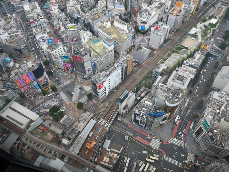 High-angle aerial view of dense Tokyo urban area from Shibuya Sky, showing buildings, complex road networks with traffic, and train tracks winding through the city, Shibuya, Tokyo, Japan.