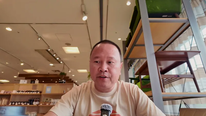 Man in beige shirt and glasses seated in a cafe in Tokyo, Japan, speaking to camera.