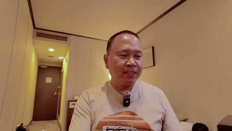 Man in beige shirt and glasses speaking to camera in a Tokyo hotel room, holding a Sony camera box, Tokyo, Japan.