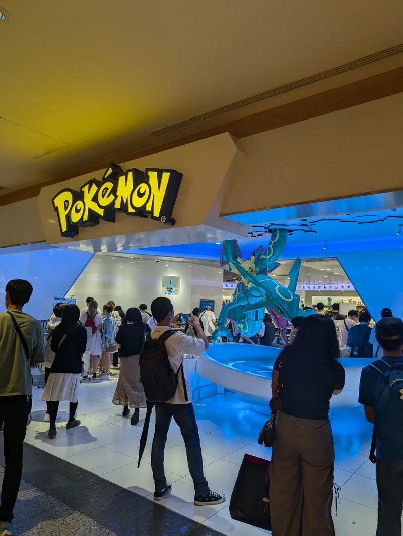 Entrance to the Pokémon Center at Solamachi in the Tokyo Skytree complex, with a large illuminated Pokémon logo and a prominent Rayquaza statue, crowds of visitors gathered outside, Tokyo, Japan.