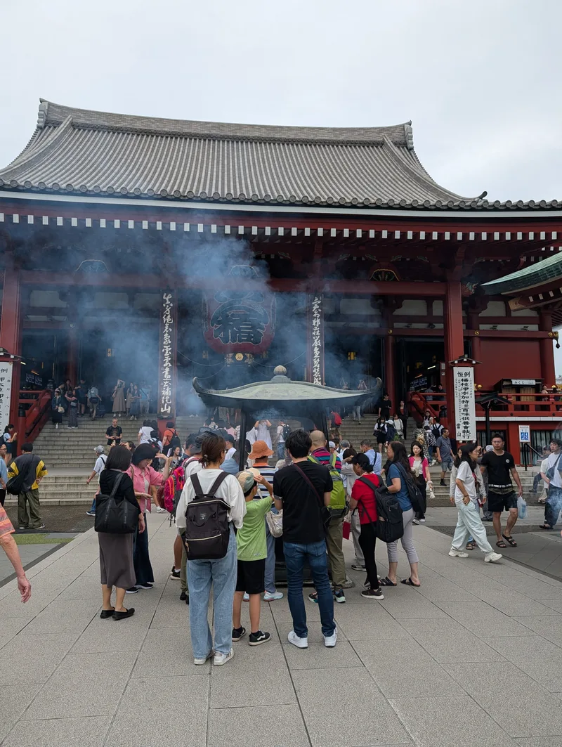Tourists gathered around a large incense burner with thick smoke billowing at Senso-ji Temple in Asakusa, Tokyo, Japan.