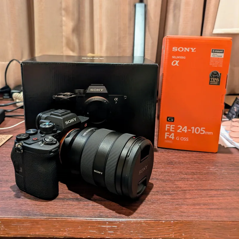 Brand-new Sony Alpha 7 IV camera with FE 24-105mm F4 G OSS lens displayed alongside their packaging boxes on a wooden table, Tokyo, Japan.