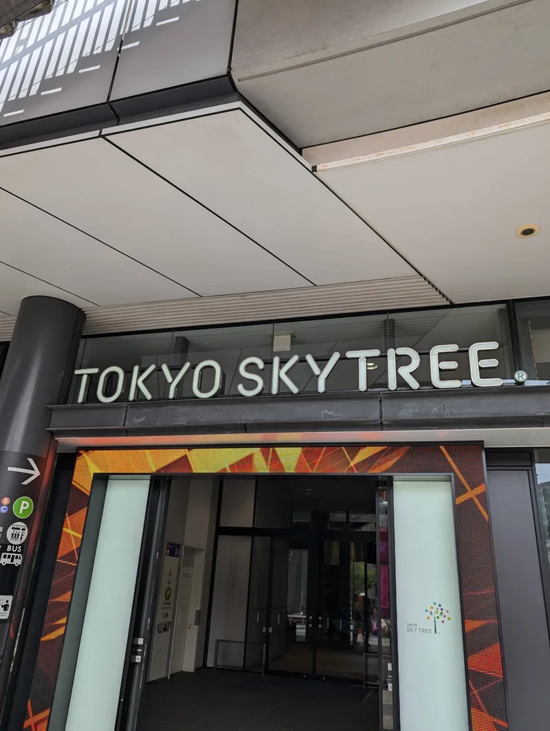 Entrance to the Tokyo Skytree complex with illuminated TOKYO SKYTREE sign and directional transport icons, Tokyo, Japan.