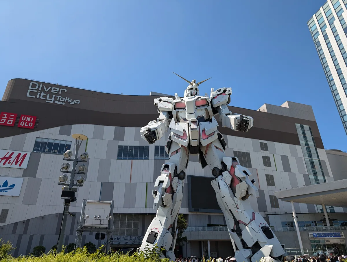 Life-sized Unicorn Gundam statue in white and red standing in front of DiverCity Tokyo Plaza mall under a clear blue sky, Odaiba, Tokyo, Japan.