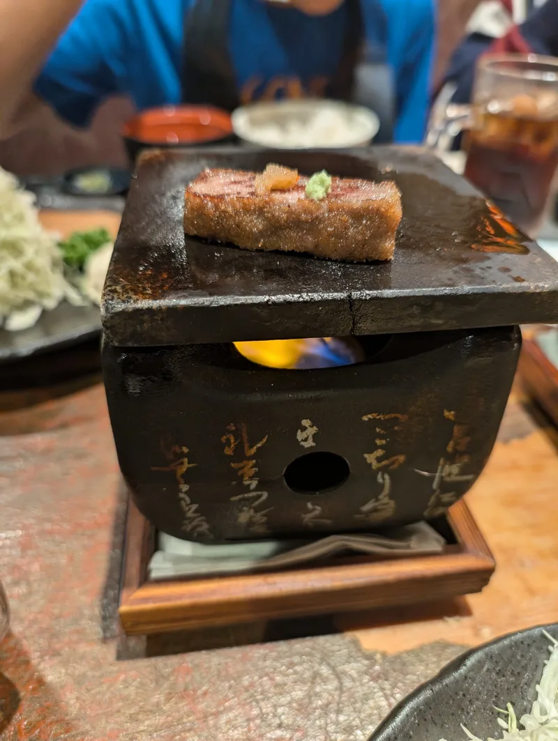 Wagyu beef cooking on a personal stone grill with a flame underneath at a Japanese restaurant in Tokyo, Japan, with a small dollop of green condiment on top.