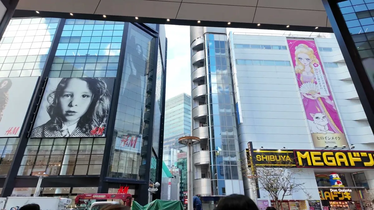 Street-level view of Shibuya with the Mega Don Quijote sign, H&M billboard, and anime advertisements on buildings in Tokyo, Japan