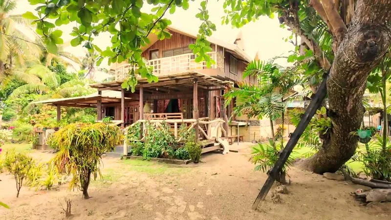 The main house — my brother-in-law and I stayed in this exact room 11 years ago Two-story wooden beach house with porch and balcony surrounded by tropical trees at Uncle Henry's resort in Roxas, Palawan