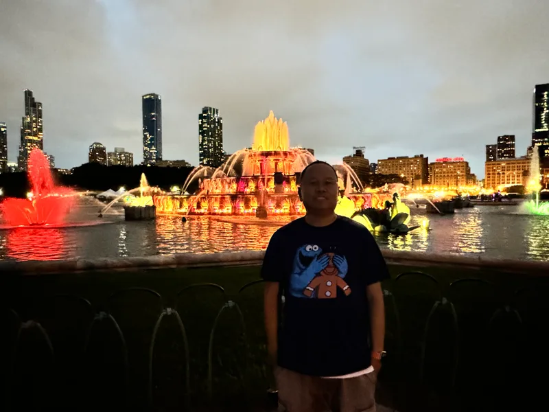 Man standing in front of Buckingham Fountain illuminated with colorful lights at dusk in Chicago, Illinois